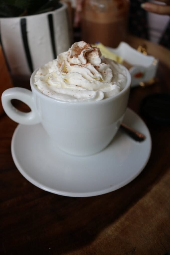 Whipped cream topped cappuccino in a white cup on a wooden table, perfect for cozy moments.